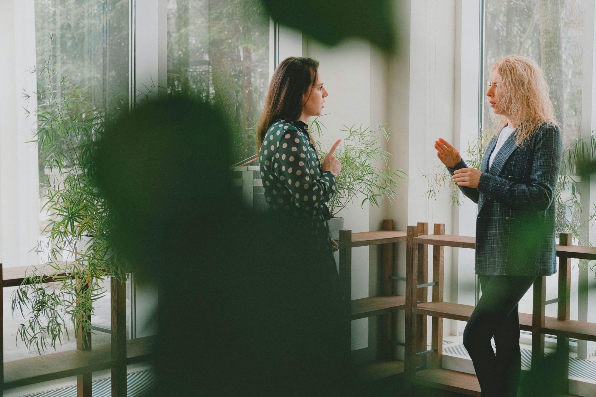Two women in conversation in a bright room full of plants